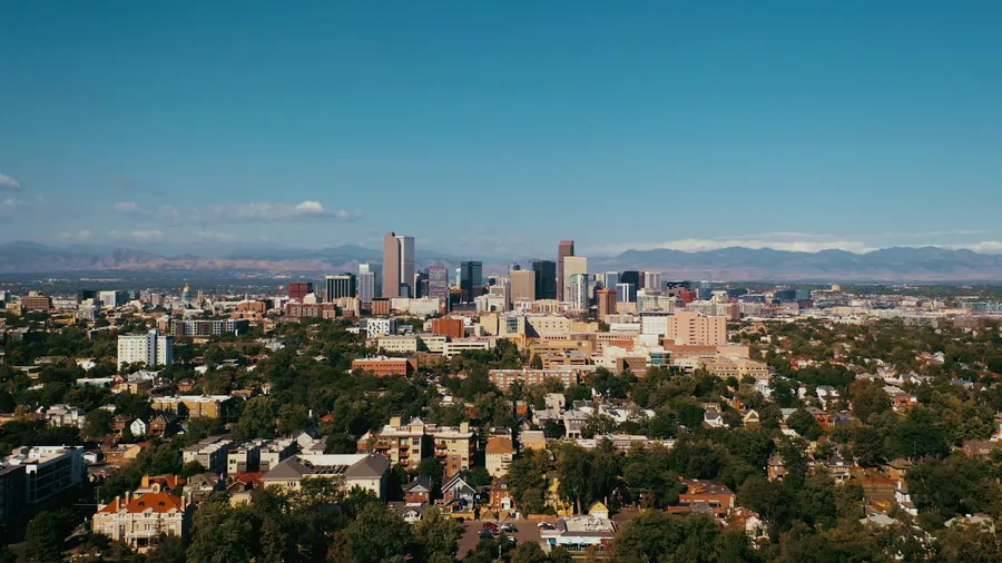 Aerial view of a leafy Denver, Colorado neighborhood with the downtown skyline and Rocky Mountains in the distance