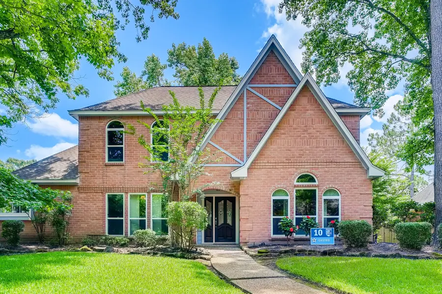 A two-story brick home with a lush green front lawn on a sunny day